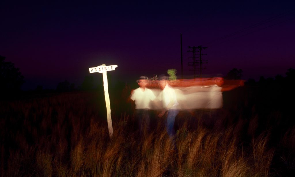 A photograph taken at night which highlights a sign that says 'Prairie' and the blur of a person moving sideways.
