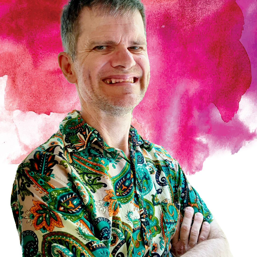 2024 Access Arts Achievement Award Winner - Michael Russell. Michael is facing the camera with his arms crossed. He is wearing a colourful Hawaiian shirt and he is smiling at the camera.